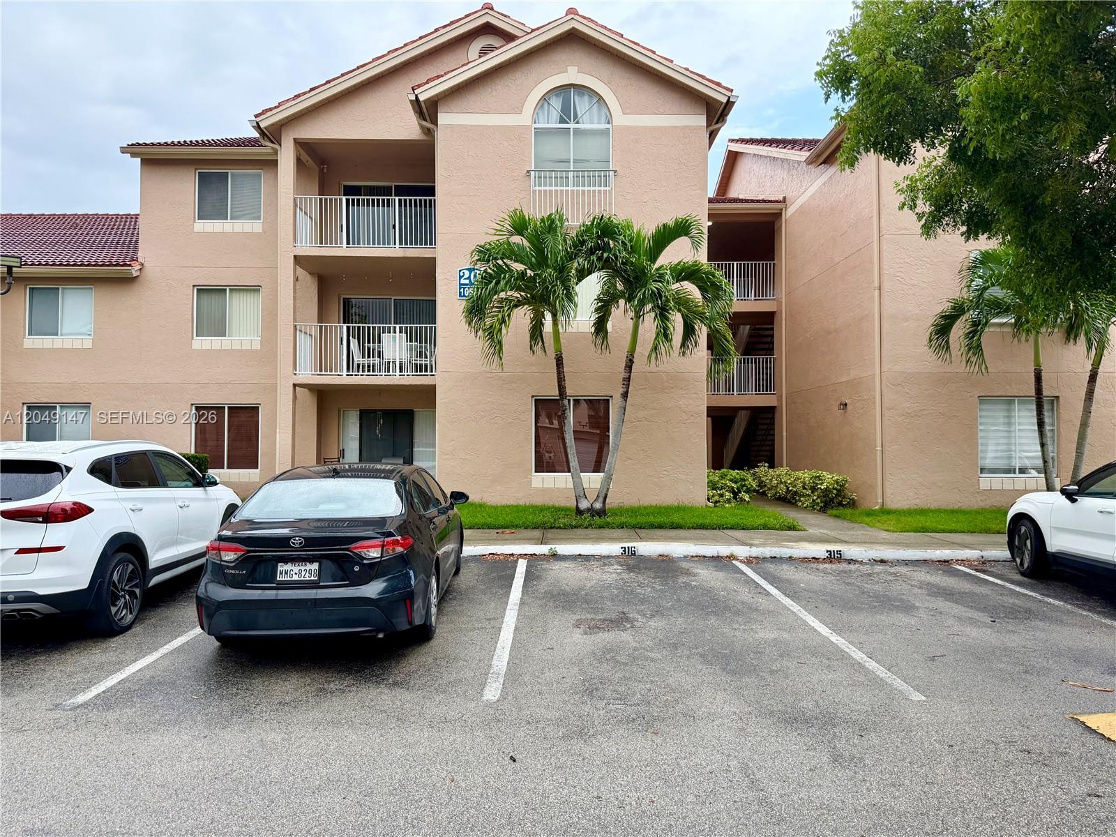 A multi-story tan apartment building features balconies, palm trees, and a parking lot in front — 10521 SW 158th Ct # 203, Miami FL 33196, MIAMI, FL