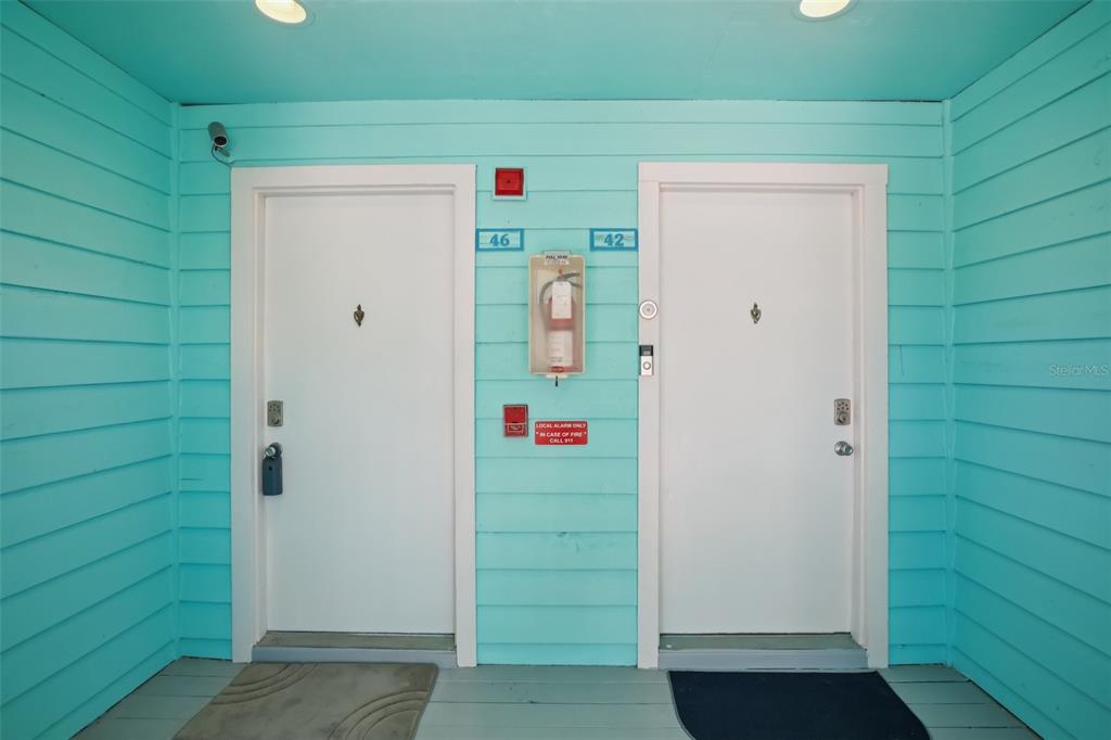 Two white doors with unit numbers 46 and 42 sit on a teal-sided exterior porch — 455 ALT 19 S UNIT 42 & 46, PALM HARBOR, FL