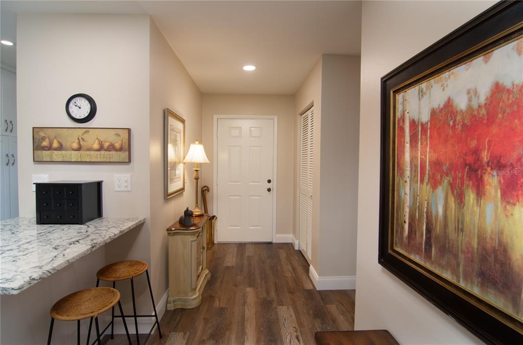 An entryway features wood-look flooring, a white door, a granite countertop, and wall art — 5635 GOLF POINTE DRIVE UNIT 101, SARASOTA, FL