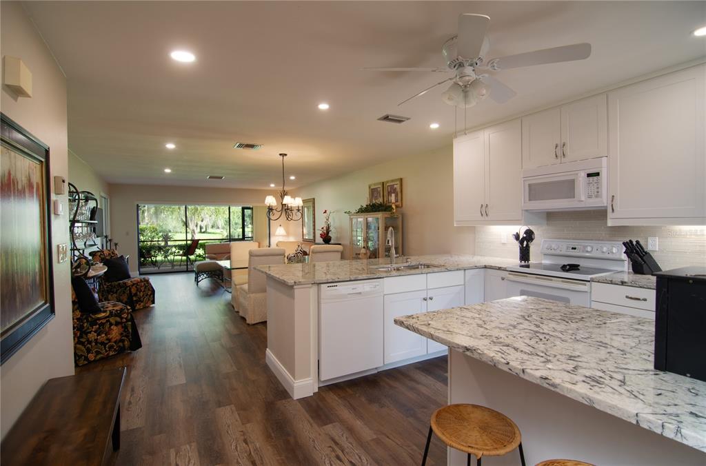 A kitchen with white cabinets and granite countertops opens into a living and dining area — 5635 GOLF POINTE DRIVE UNIT 101, SARASOTA, FL