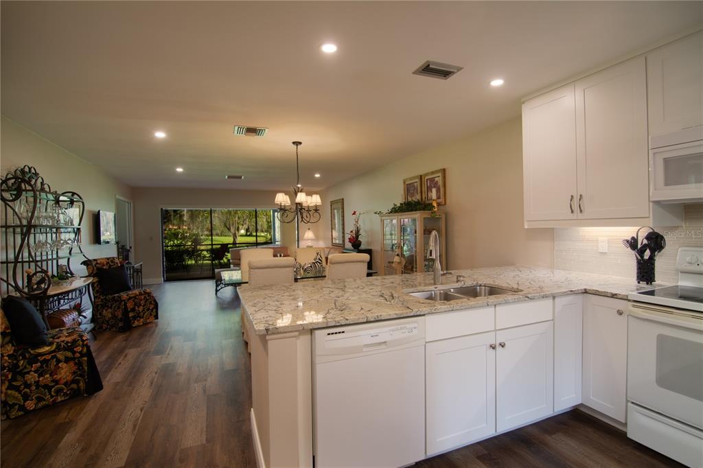 A kitchen with white cabinets and granite countertops overlooks an open-concept dining and living area — 5635 GOLF POINTE DRIVE UNIT 101, SARASOTA, FL