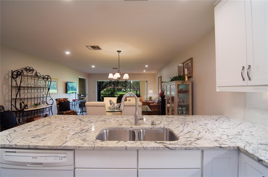 A kitchen island with a granite countertop and double sink overlooks an open dining area — 5635 GOLF POINTE DRIVE UNIT 101, SARASOTA, FL