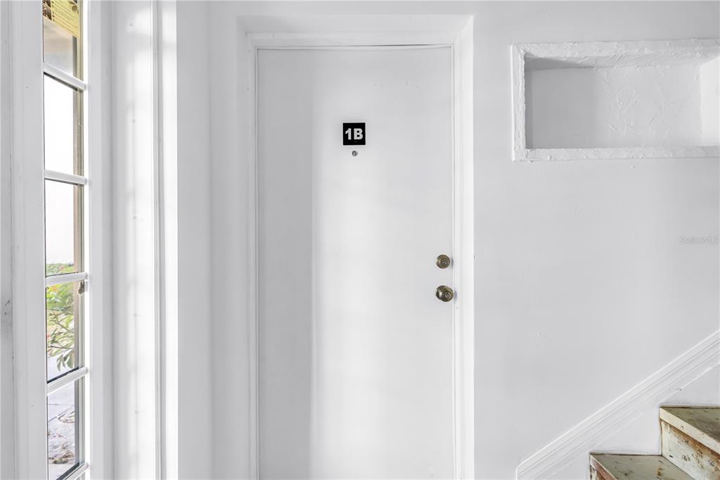 A white door labeled 1B is positioned next to a window and a staircase — 6960A SUNSET DRIVE S UNIT 1B, SOUTH PASADENA, FL