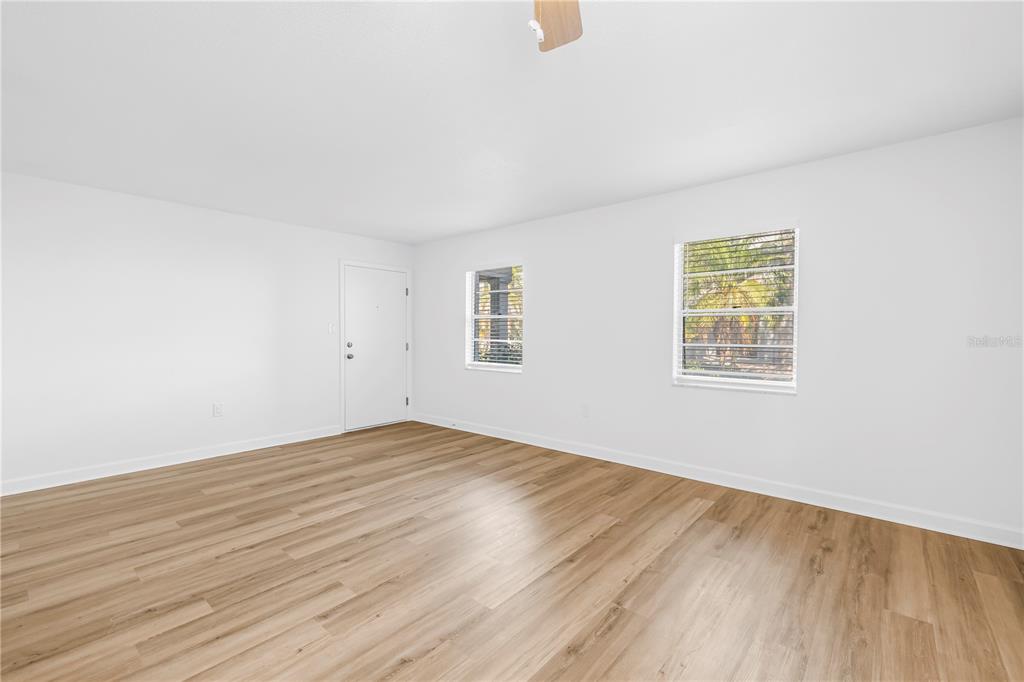 An empty room features white walls, light wood-look flooring, and two windows with blinds — 6960A SUNSET DRIVE S UNIT 1B, SOUTH PASADENA, FL