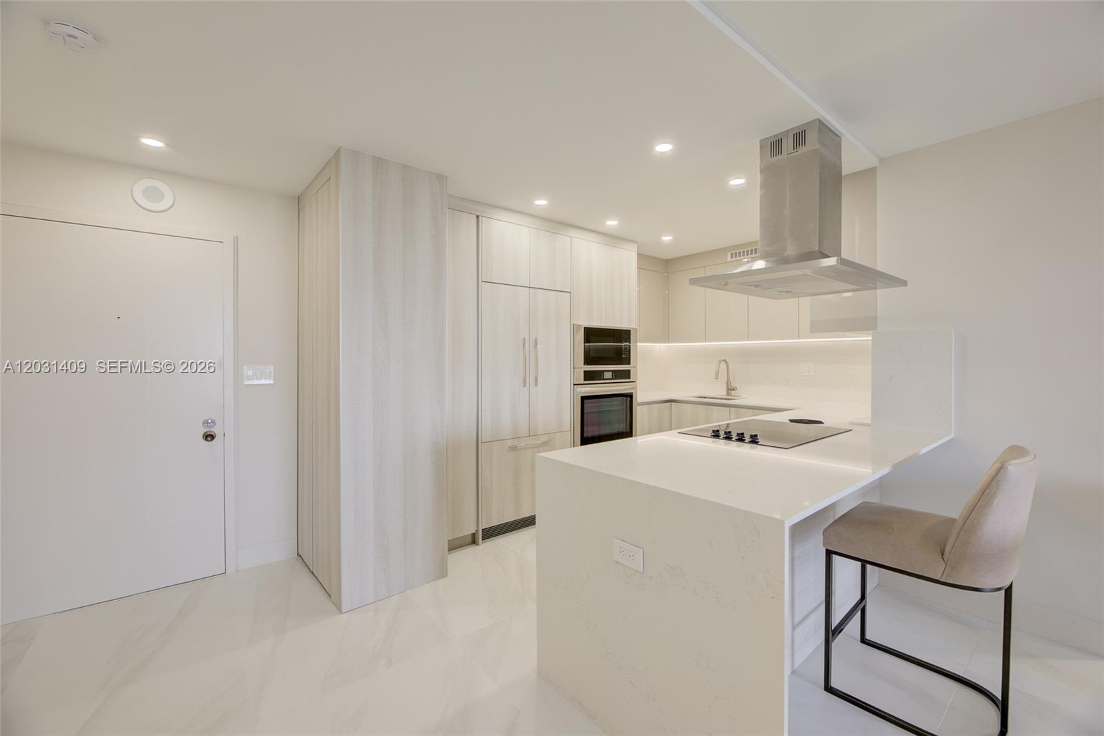 A modern kitchen features light wood cabinetry, white quartz countertops, and a stainless steel hood — 600 Three Islands Blvd # 403, Hallandale Beach FL 33009, HALLANDALE BEACH, FL
