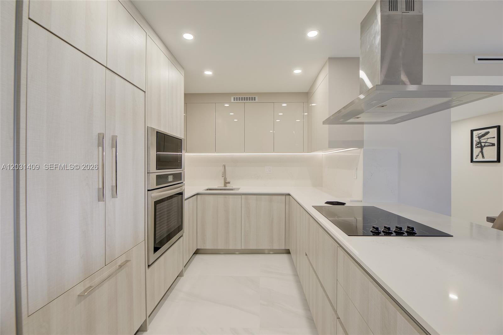 A modern kitchen features light wood cabinetry, white countertops, stainless steel appliances, and recessed lighting — 600 Three Islands Blvd # 403, Hallandale Beach FL 33009, HALLANDALE BEACH, FL