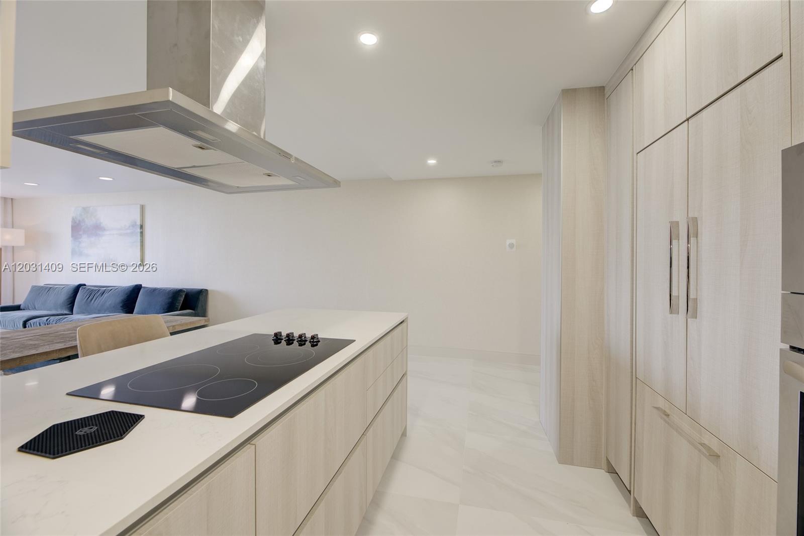 A modern kitchen features a central island with a cooktop and light wood cabinetry — 600 Three Islands Blvd # 403, Hallandale Beach FL 33009, HALLANDALE BEACH, FL