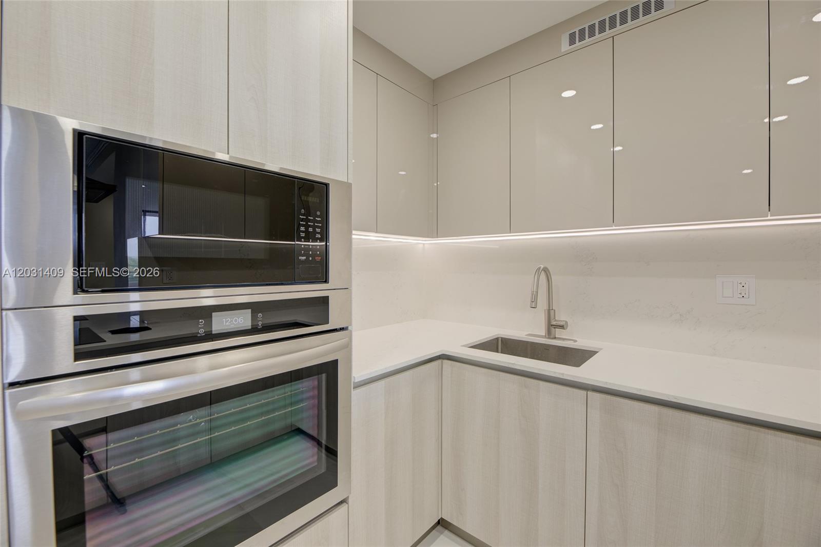 A modern kitchen features light wood cabinetry, white countertops, a stainless steel sink, and built-in appliances — 600 Three Islands Blvd # 403, Hallandale Beach FL 33009, HALLANDALE BEACH, FL