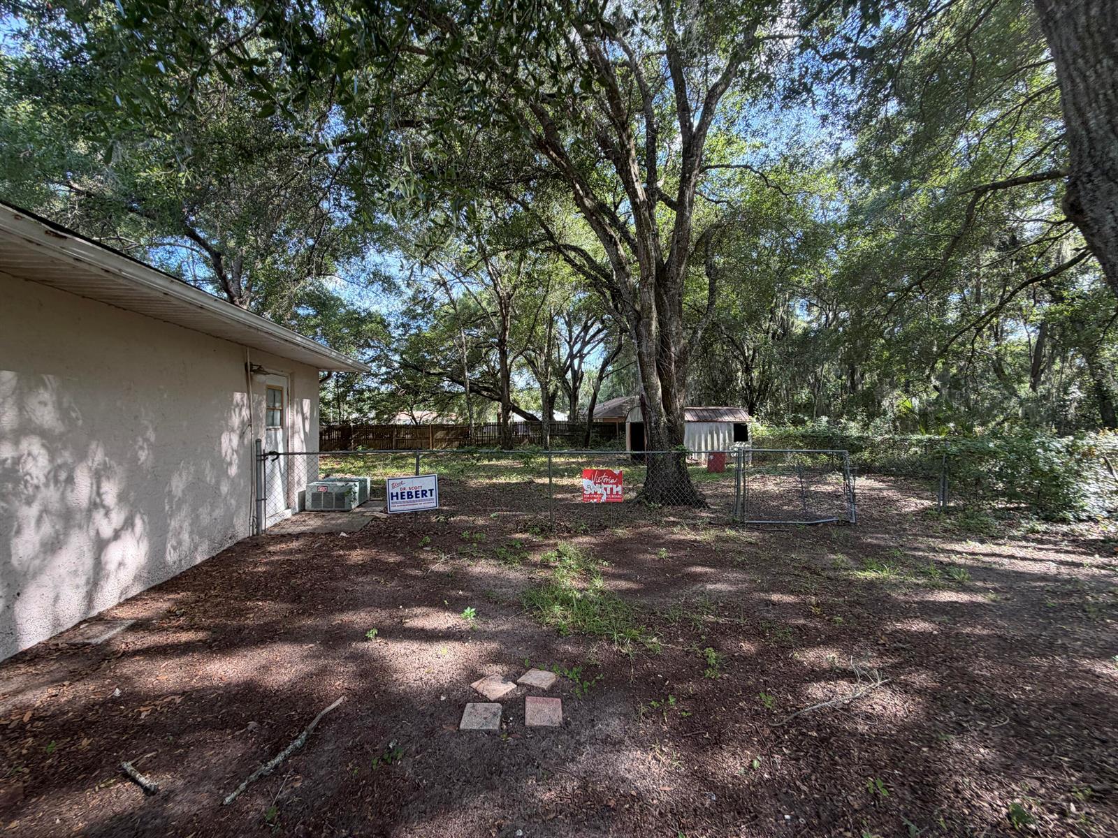 A fenced backyard features a house exterior, mature trees, and a small storage shed — 3920 E Allendale Street, Inverness FL 34453, INVERNESS, FL