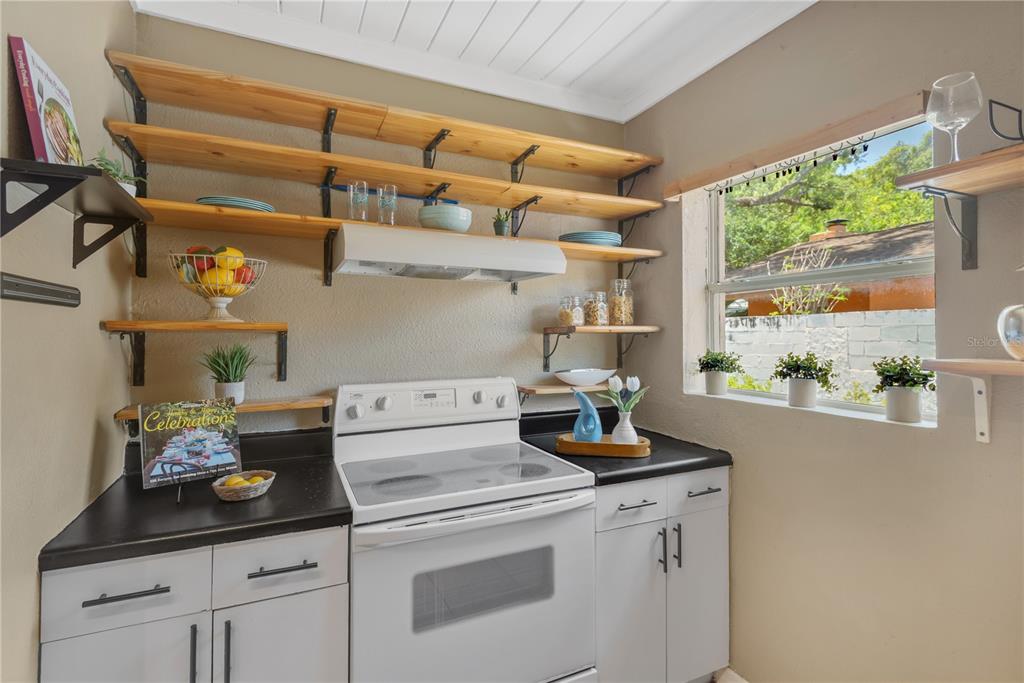 A kitchen features white cabinets, black countertops, open wood shelving, and a white electric stove — 1315 E OSBORNE AVENUE, TAMPA, FL