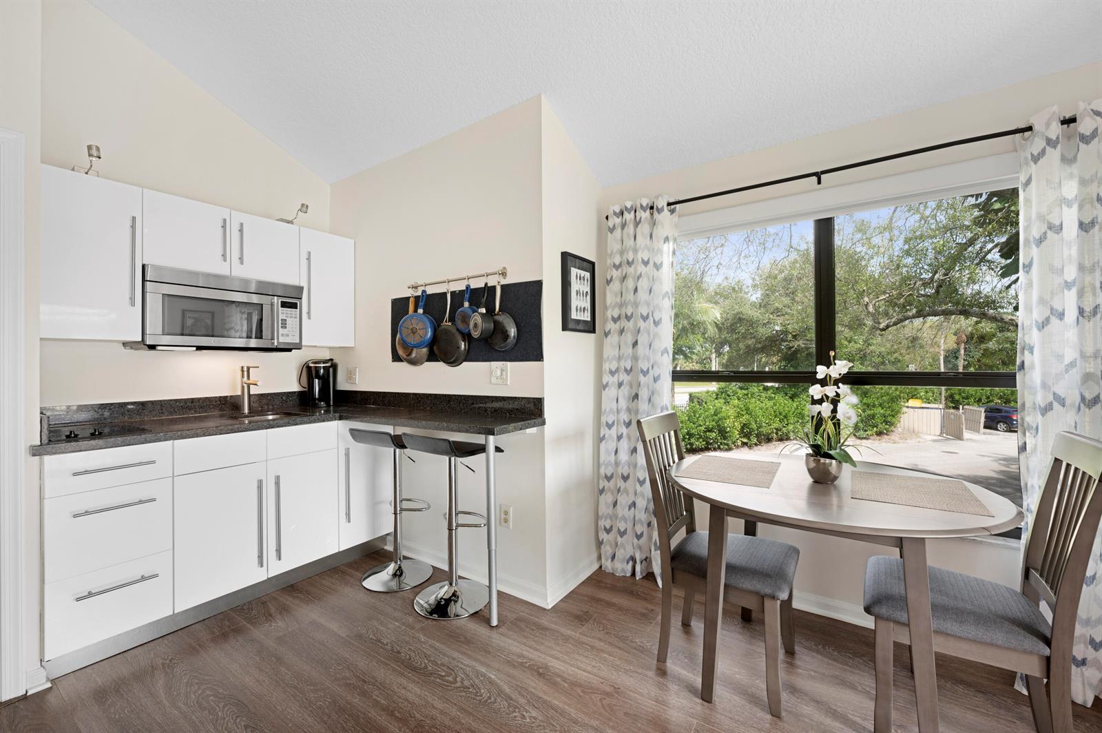 A kitchen with white cabinets, a breakfast bar, and a dining table by a window — 11863 Wimbledon Circle # 543, Wellington FL 33414, WELLINGTON, FL