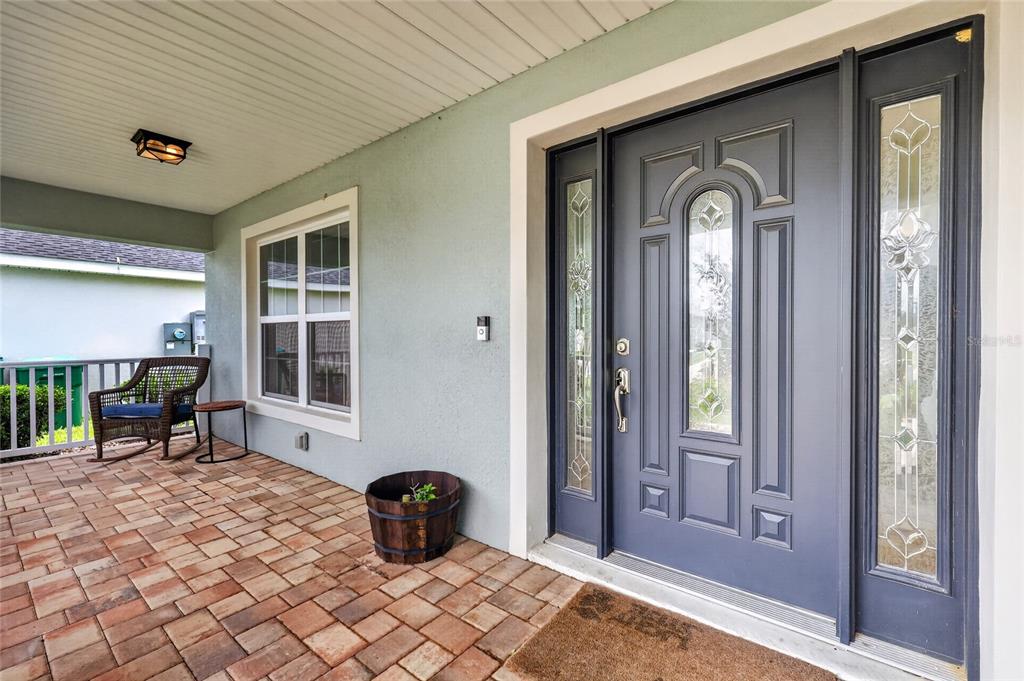 A covered porch features a gray front door with sidelights, a wicker chair, and pavers — 12591 NE 49TH DRIVE, OXFORD, FL