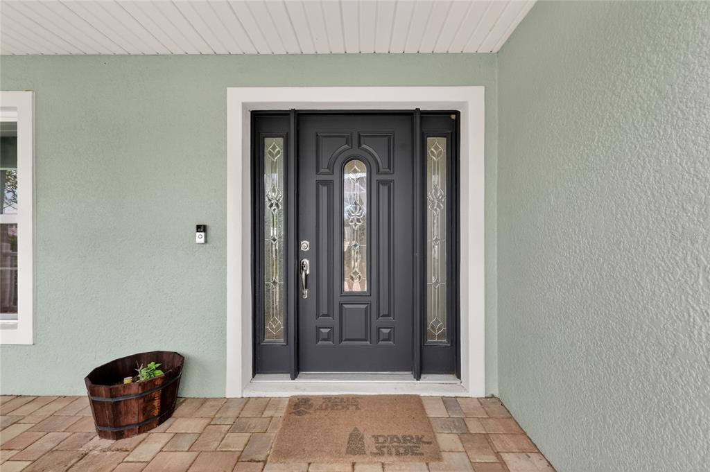 A dark gray front door with glass sidelights sits on a porch with tiled flooring — 12591 NE 49TH DRIVE, OXFORD, FL