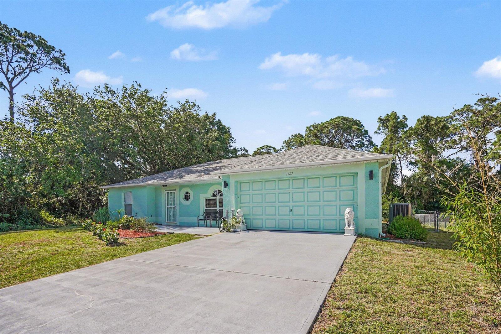 A light green single-story house features a two-car garage, a concrete driveway, and landscaping — 1367 Wing Road SW, Palm Bay FL 32908, PALM BAY, FL