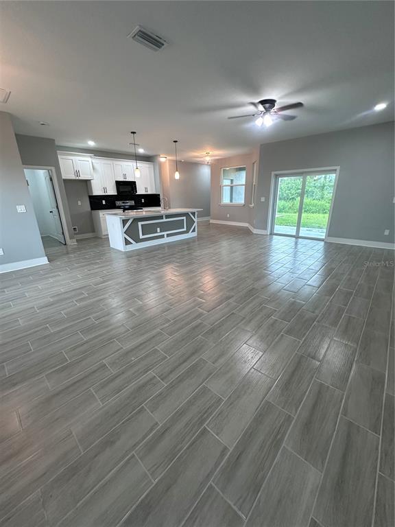 An open-concept kitchen and living area features gray wood-look tile flooring and white cabinetry — 13195 DRYSDALE AVENUE, PORT CHARLOTTE, FL