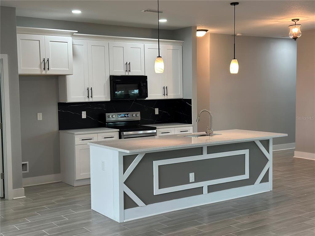 A modern kitchen features white cabinets, a black marble backsplash, and a gray-accented kitchen island — 13195 DRYSDALE AVENUE, PORT CHARLOTTE, FL