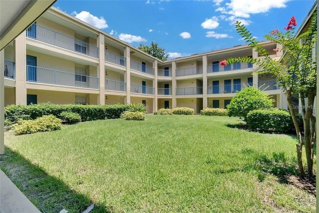 A multi-story apartment building exterior features a central grassy courtyard with manicured landscaping — 7310 WESTPOINTE BOULEVARD UNIT 623, ORLANDO, FL