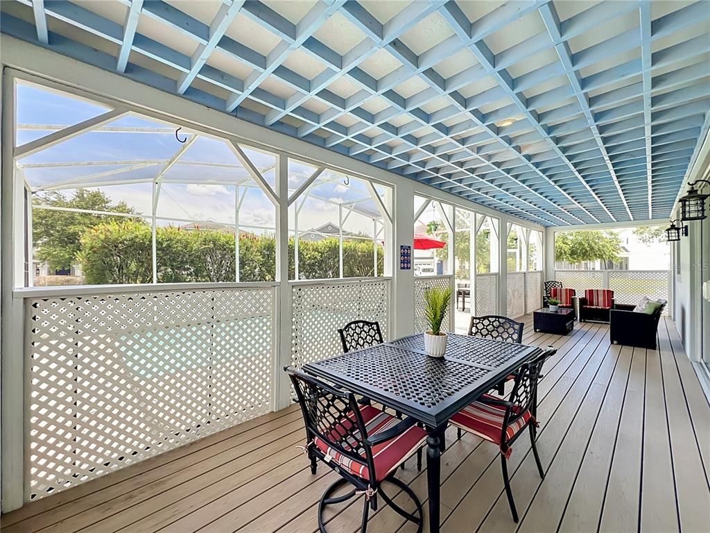 A screened-in porch features a wooden deck, a dining set, and a blue lattice ceiling — 1573 MAIDSTONE COURT, DAVENPORT, FL