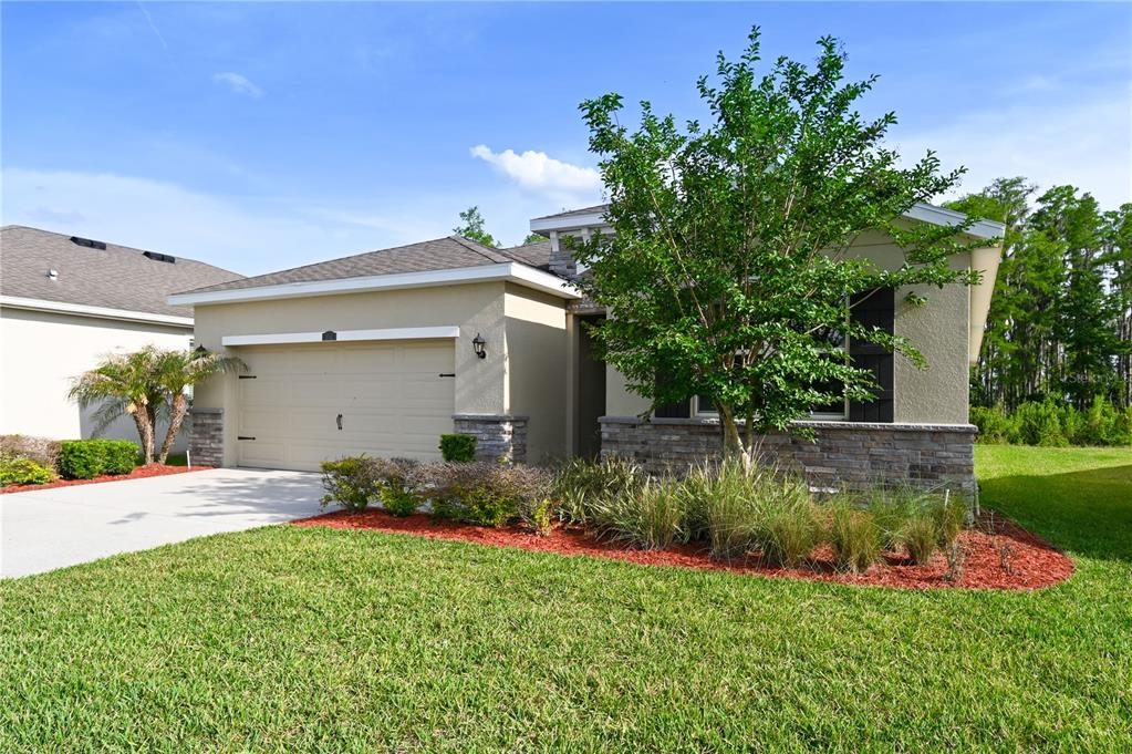 A single-story house with a beige stucco exterior, stone accents, and a two-car garage — 1052 MANZANAR PLACE, WESLEY CHAPEL, FL