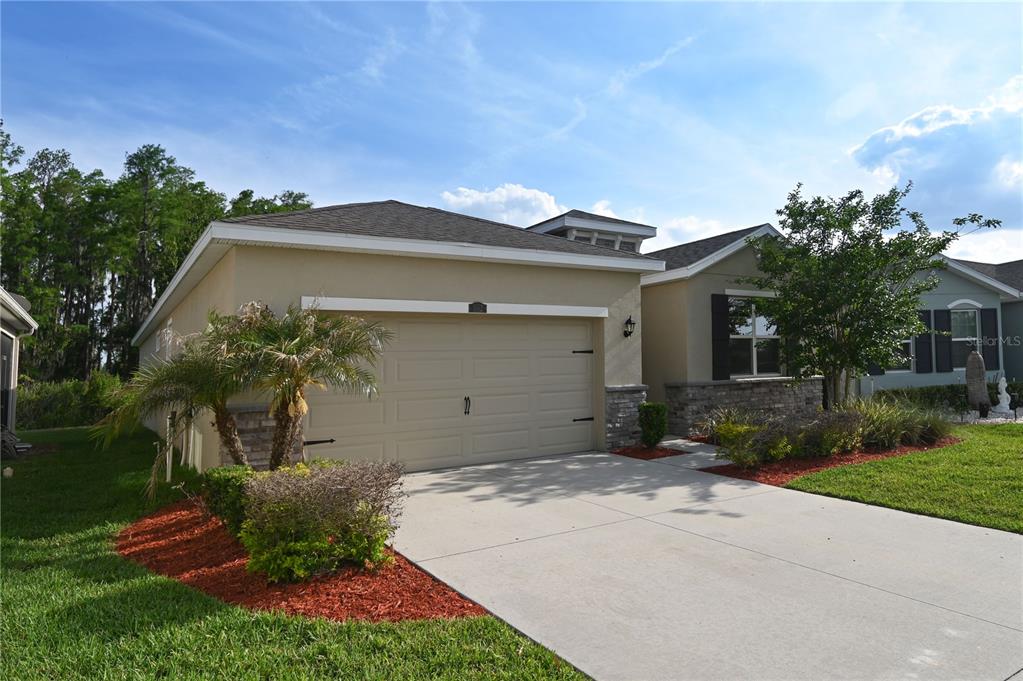 A tan single-story house with a two-car garage, stone accents, and a concrete driveway — 1052 MANZANAR PLACE, WESLEY CHAPEL, FL