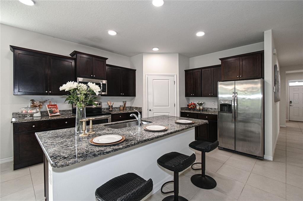 A kitchen features dark wood cabinets, granite countertops, a center island, and stainless steel appliances — 1052 MANZANAR PLACE, WESLEY CHAPEL, FL