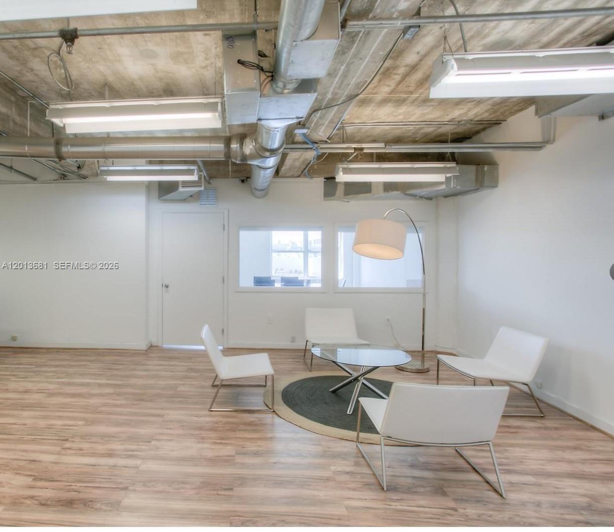 A modern office lounge features white chairs, a glass table, and exposed industrial ceiling ducts — 605 Lincoln Rd # 460, Miami Beach FL 33139, MIAMI BEACH, FL