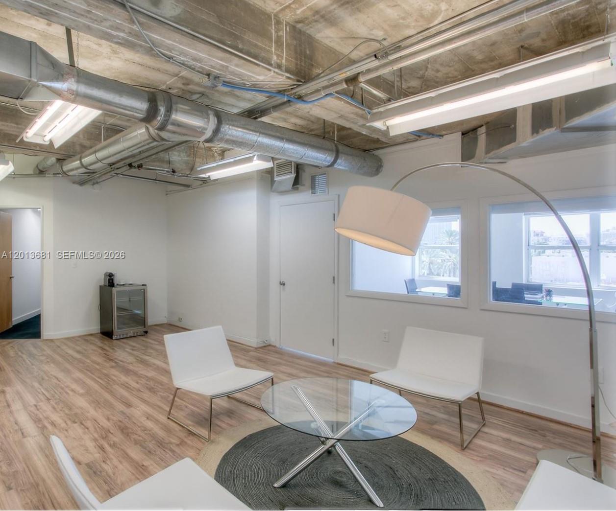A modern office waiting area features exposed ceiling ducts, white chairs, and a glass table — 605 Lincoln Rd # 460, Miami Beach FL 33139, MIAMI BEACH, FL