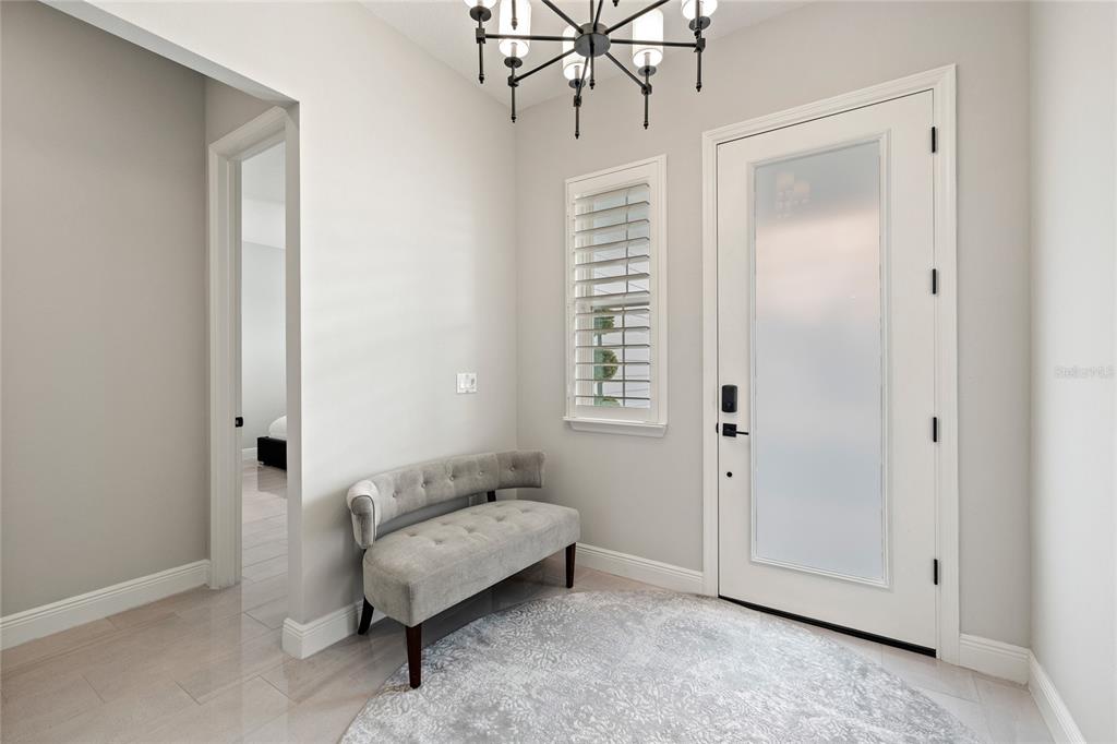 A bright entryway features a gray tufted bench, a round rug, and a modern chandelier — 3126 VANGUARD COURT, ST CLOUD, FL