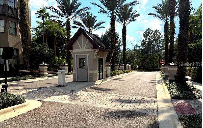 A gated entrance features a small guardhouse, palm trees, and a paved driveway — 14501 GROVE RESORT AVENUE UNIT 1105, WINTER GARDEN, FL
