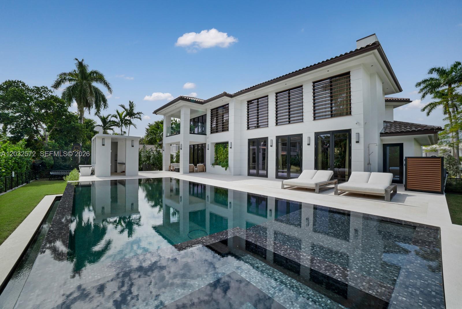A modern two-story white house features a large infinity pool and two lounge chairs — 199 Caoba Ct, Coral Gables FL 33143, CORAL GABLES, FL