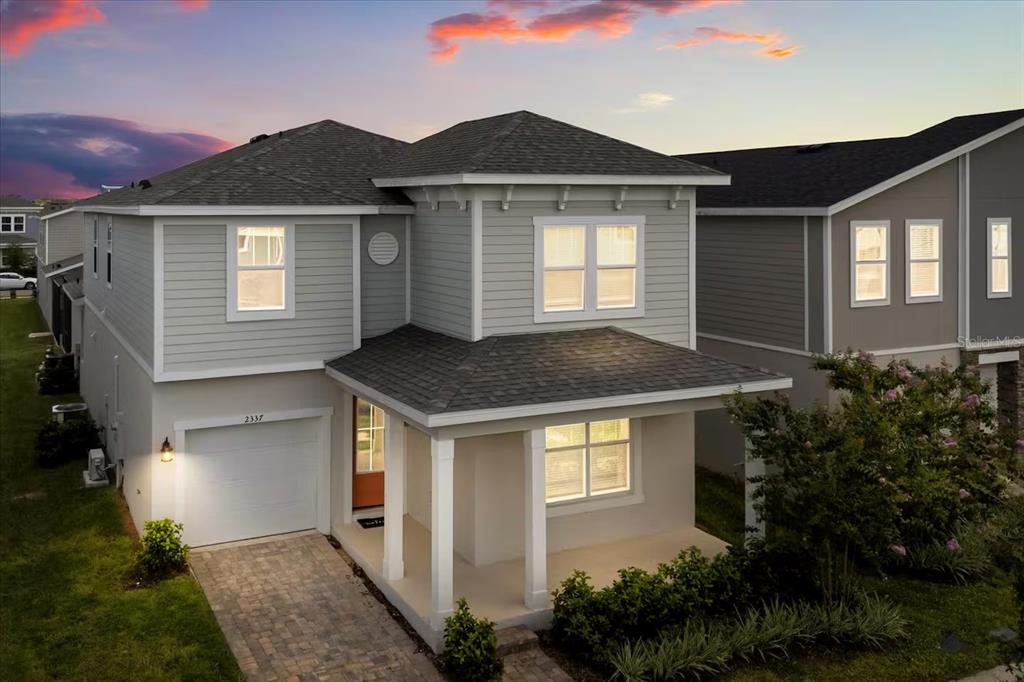 A two-story gray house with a paved driveway and a covered front porch at dusk — 2337 SALTY WINDS WAY, KISSIMMEE, FL