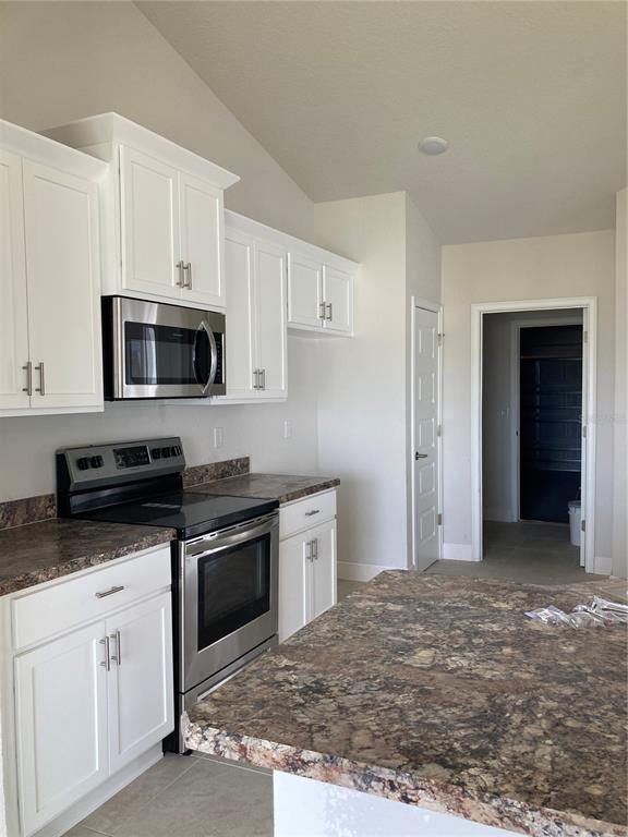 A kitchen features white cabinets, stainless steel appliances, and a dark granite countertop island — 12609 NE 48TH STREET, OXFORD, FL