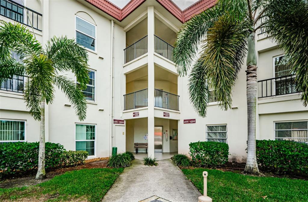 The exterior of a multi-story apartment building features balconies, palm trees, and a central walkway — 2700 BAYSHORE BOULEVARD UNIT 3310, DUNEDIN, FL