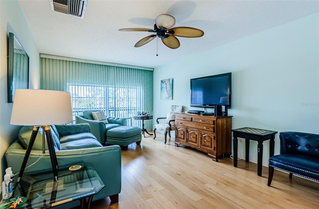 A living room features light blue walls, hardwood floors, a ceiling fan, and teal furniture — 2700 BAYSHORE BOULEVARD UNIT 3310, DUNEDIN, FL