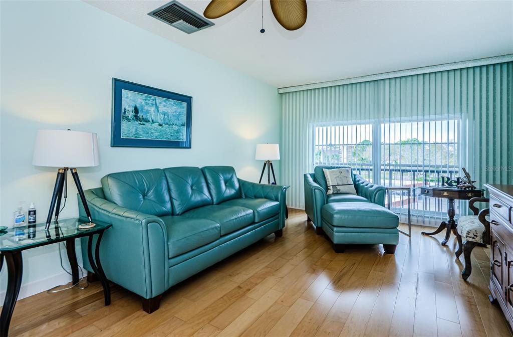 A living room features a teal leather sofa and matching chaise lounge on hardwood floors — 2700 BAYSHORE BOULEVARD UNIT 3310, DUNEDIN, FL