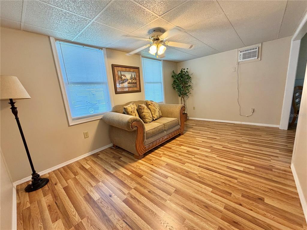 A living room features wood-look flooring, a beige sofa, two windows, and a ceiling fan — 115 GARDENIA WAY, LEESBURG, FL