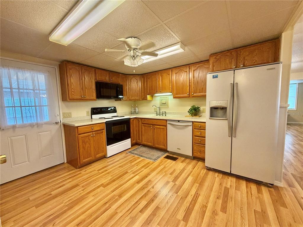 A kitchen features wood cabinets, white appliances, and light-colored wood-look flooring — 115 GARDENIA WAY, LEESBURG, FL