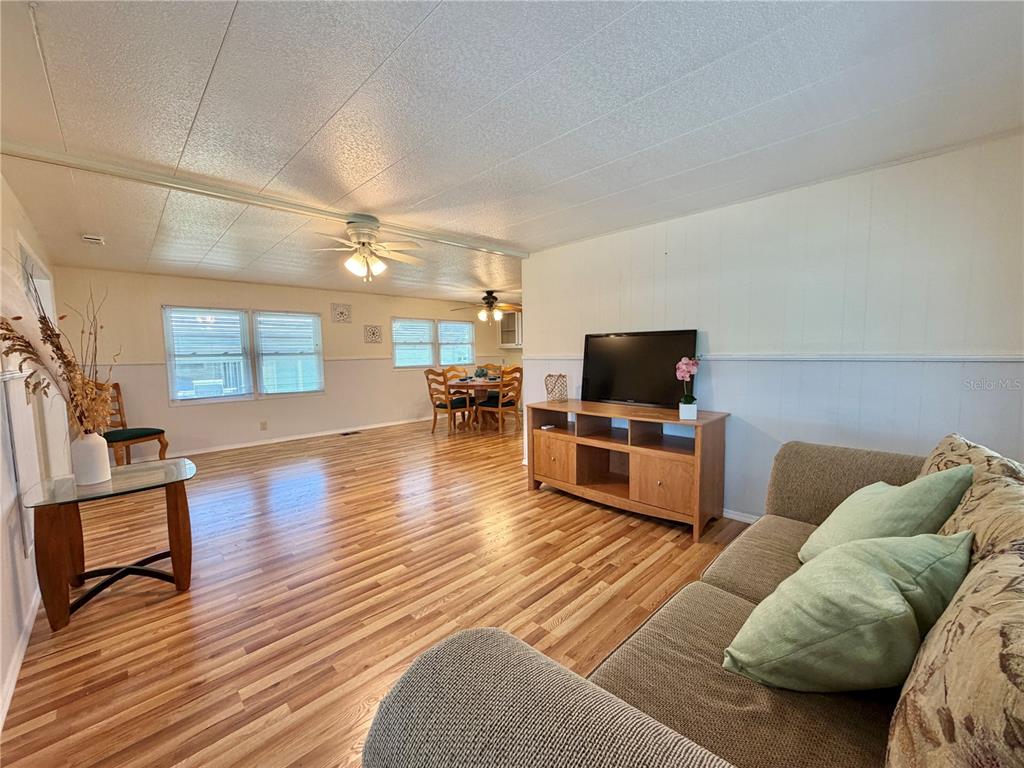 A living room with wood-look flooring, a television console, and an adjacent dining area — 115 GARDENIA WAY, LEESBURG, FL