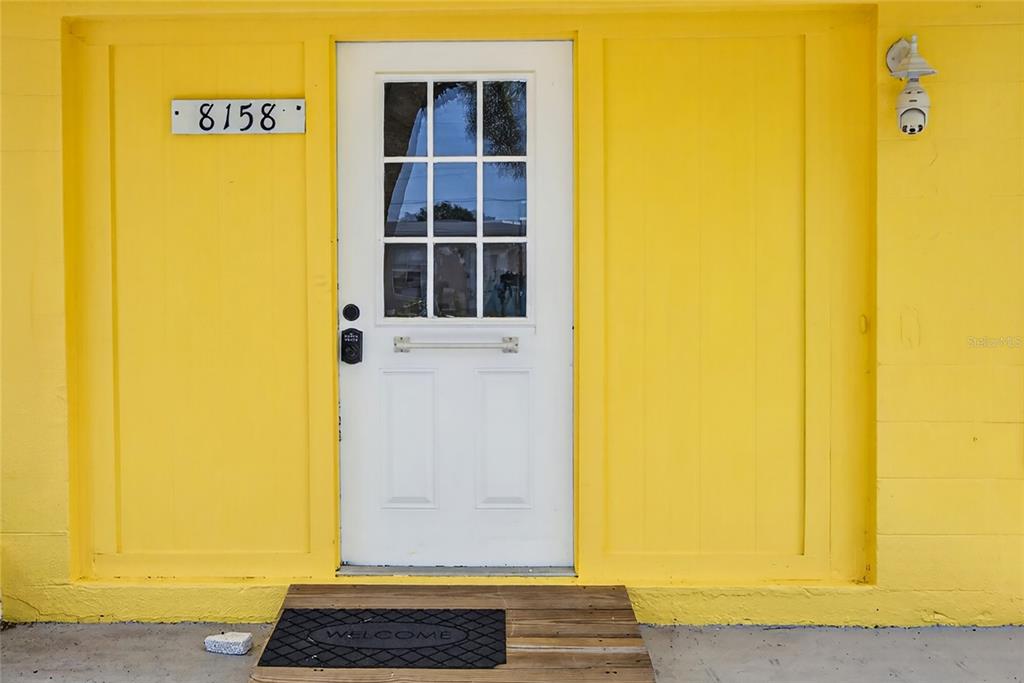 A white door with a nine-pane window is centered on a bright yellow exterior wall — 8158 AGRESS AVENUE, NORTH PORT, FL