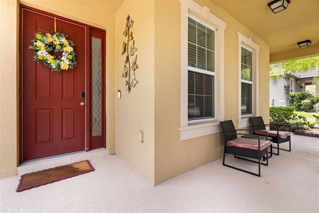 A red front door with a floral wreath sits beside two chairs on a porch — 3737 CHANDLER ESTATES DRIVE, APOPKA, FL