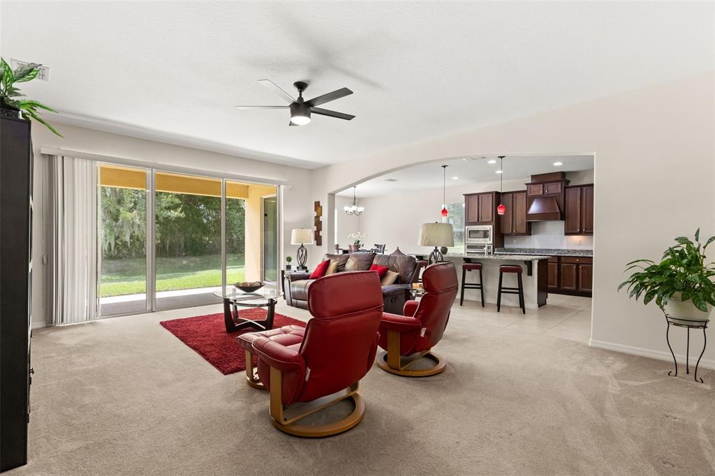 An open-concept living room and kitchen feature carpeted floors, red leather chairs, and sliding doors — 3737 CHANDLER ESTATES DRIVE, APOPKA, FL