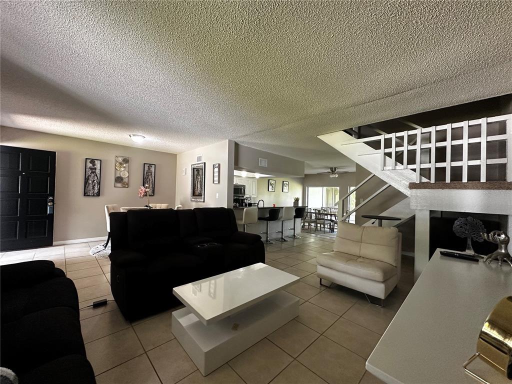A living room features tile flooring, a black sofa, a white coffee table, and a staircase — 5434 SADDLEBROOK WAY UNIT 3, WESLEY CHAPEL, FL