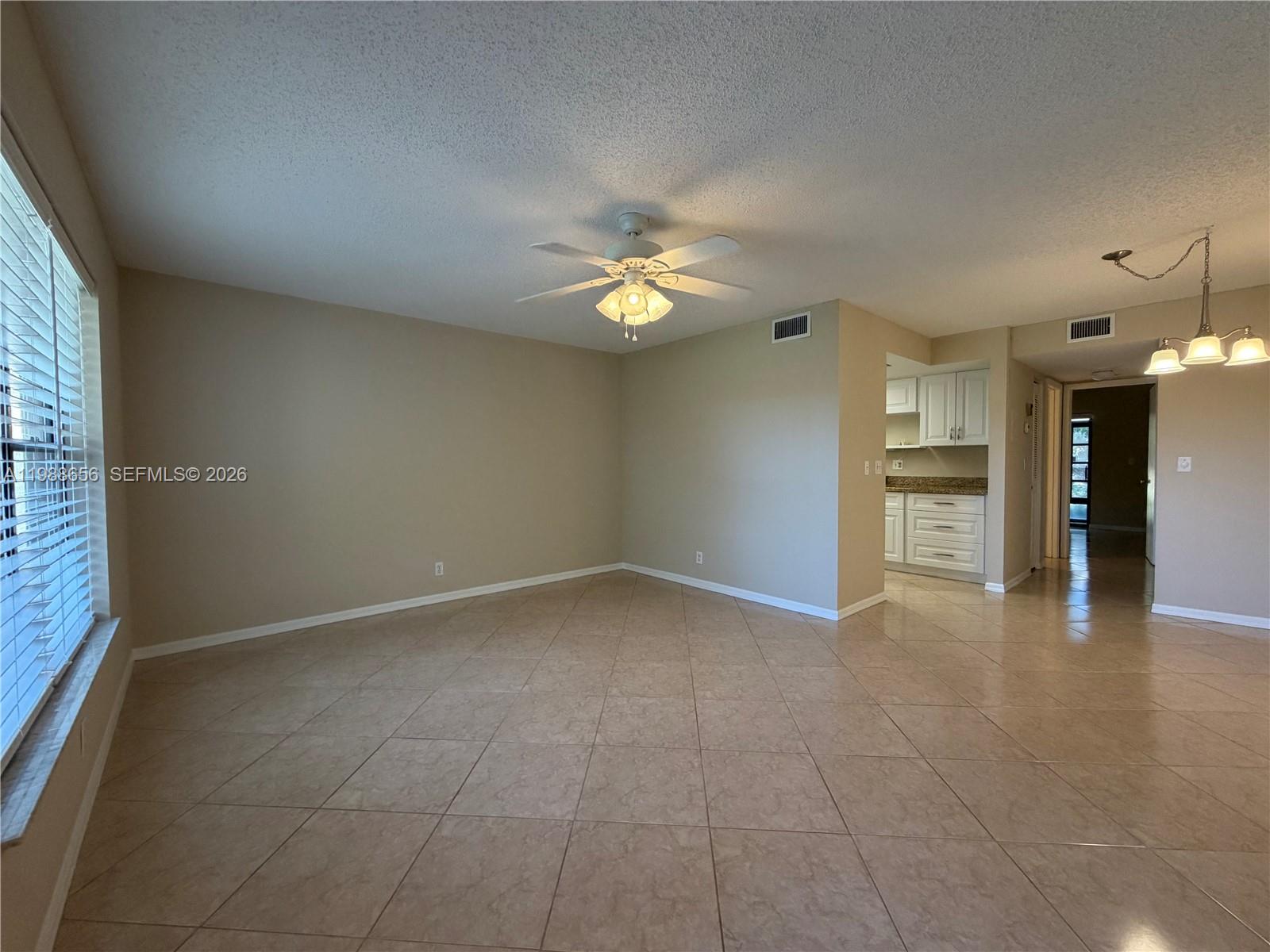 An empty living room features beige walls, tile flooring, a ceiling fan, and an adjacent kitchen — 301 SW South River Dr # 104, Stuart FL 34997, STUART, FL