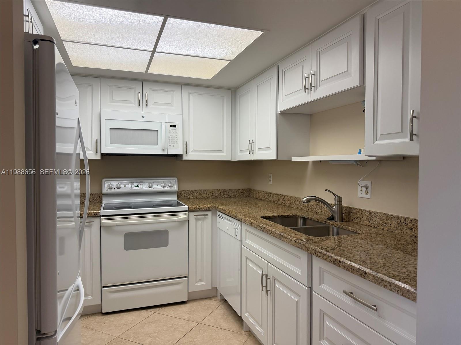 A kitchen features white cabinets, granite countertops, stainless steel sink, and white appliances — 301 SW South River Dr # 104, Stuart FL 34997, STUART, FL