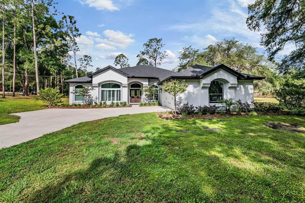 A single-story white stucco house with a dark roof and a concrete driveway — 17833 HYLAND LANE, DADE CITY, FL