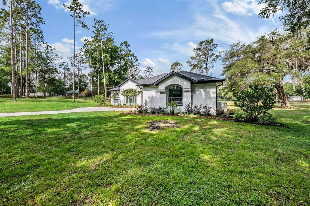 A white single-story house with a dark roof sits on a large, grassy lot — 17833 HYLAND LANE, DADE CITY, FL