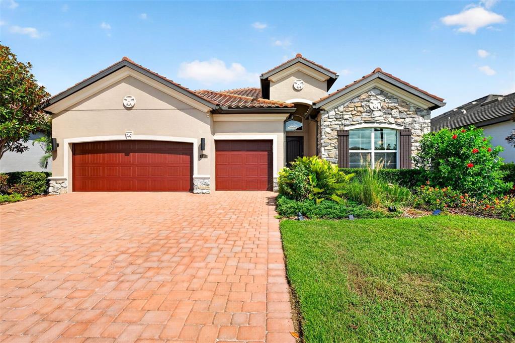 A single-story house with a stone facade, a tiled roof, and a paved driveway — 11825 PERENNIAL PLACE, BRADENTON, FL