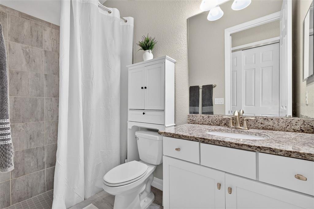 A bathroom features a granite vanity, white cabinets, a toilet with storage, and a tiled shower — 11825 PERENNIAL PLACE, BRADENTON, FL