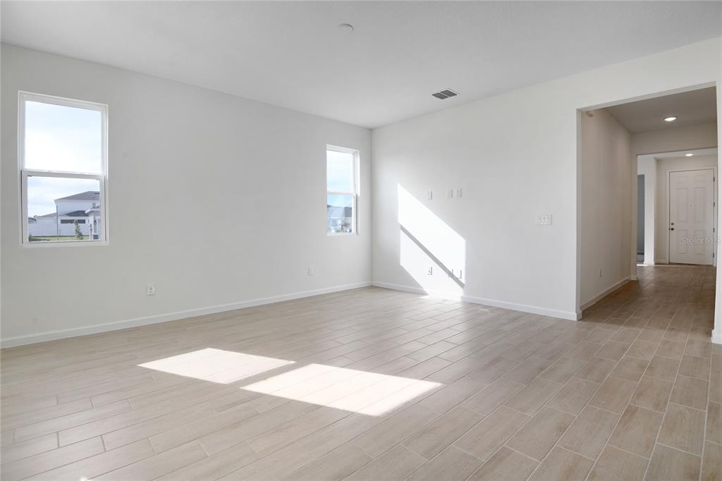 An empty living room features light-colored wood-look tile flooring, white walls, and two windows — 4056 BANNOCK AVENUE, TAVARES, FL