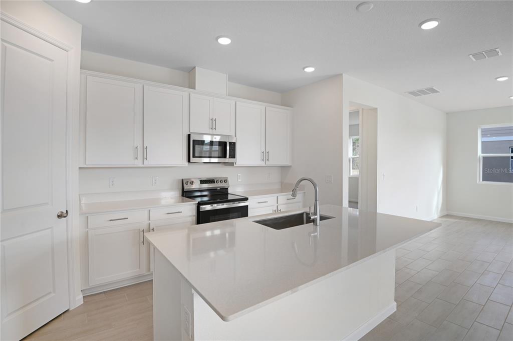 A modern kitchen features white cabinets, quartz countertops, a center island, and stainless steel appliances — 4056 BANNOCK AVENUE, TAVARES, FL